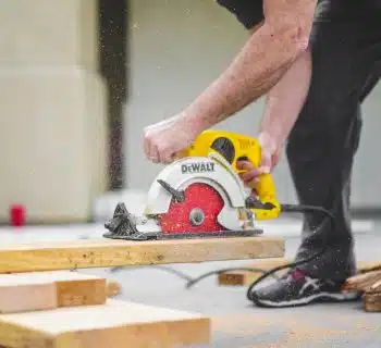 man in black sweatpants using DEWALT circular saw and cutting a wood plank