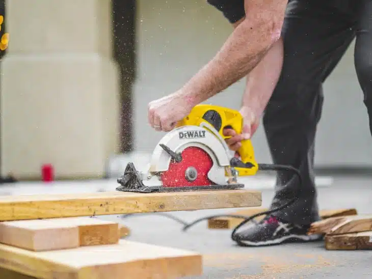 man in black sweatpants using DEWALT circular saw and cutting a wood plank